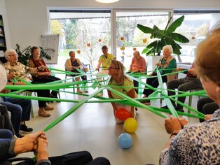 Mehre Personen sitzen in einem runden Kreis und ziehen an einem Band. 