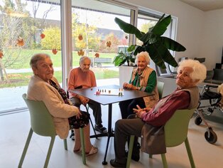 Vier Damen sitzen an einem runden Tisch und spielen Mensch ärgere dich nicht. 